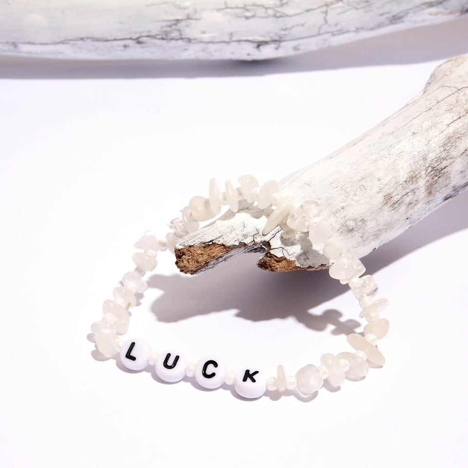 Moonstone crystal bracelet with beaded letter spelling the word 'Luck'. Bracelet is hanging from a white branch on a white background
