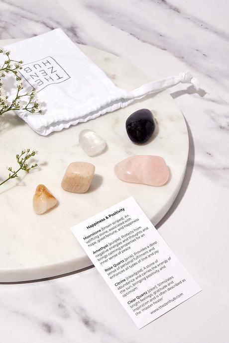 crystals aimed to help with happiness and positivity displayed on a white marble background. There is also a white drawstring bag and explanation card 