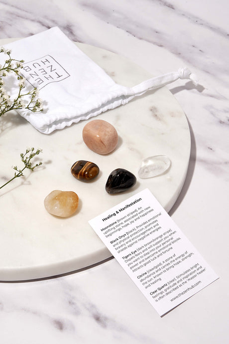 crystals aimed to help with healing and manifestation laid out of white marble background. There is also a white drawstring bag and explanation card