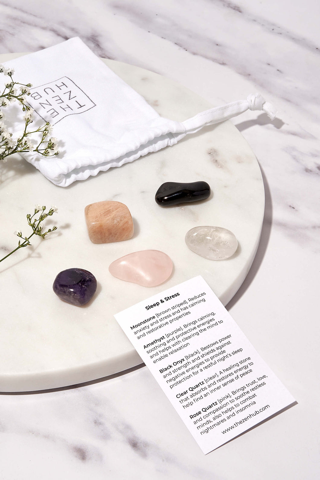 crystals designed to help with sleep and stress presented on a white marble background. There is also a white drawstring bag and explanation card beside them 
